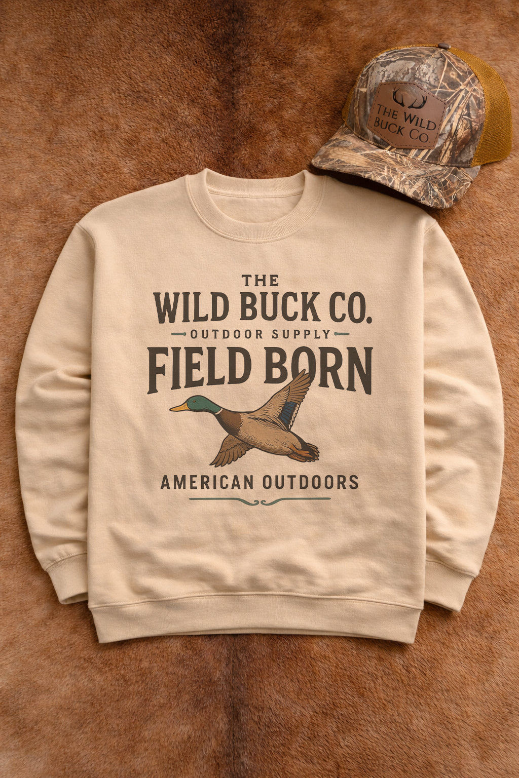 Beige sweatshirt with 'The Wild Buck Co.' branding and duck illustration on a brown leather background.