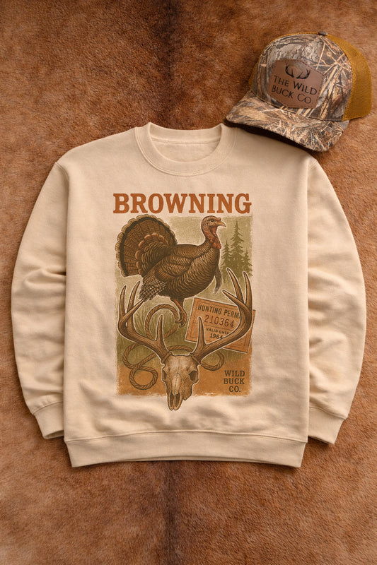 Beige sweatshirt with hunting-themed graphic and cap on a brown leather background